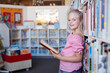 © WavebreakMediaMicro - Portrait of smiling caucasian schoolgirl standing reading book in school library