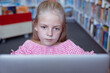 Caucasian schoolgirl at desk in school library concentrating using laptop
