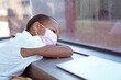 © WavebreakMediaMicro - African american schoolgirl wearing face mask sitting in school classroom looking out of window