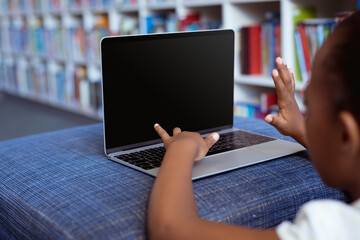 Wall Mural - African american schoolgirl at desk in school library using laptop, with copy space on screen