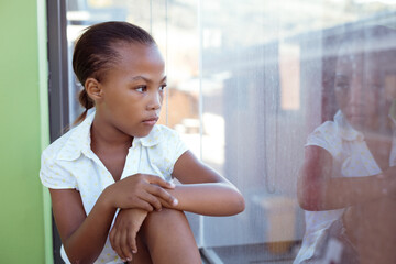 Wall Mural - African american schoolgirl sitting in school classroom looking out of window