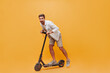 © Look! - Funny fashionable cool guy in denim shirt and grey sneakers riding scooter and having fun on isolated orange background..