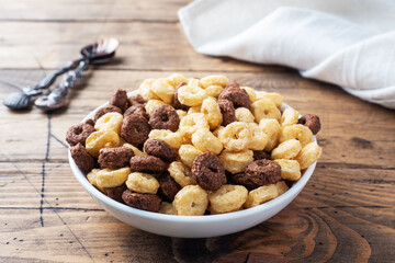 Wall Mural - Dry breakfast cereals. Chocolate and corn rings made from natural cereals with milk in a plate. Wooden rustic background, copy space.