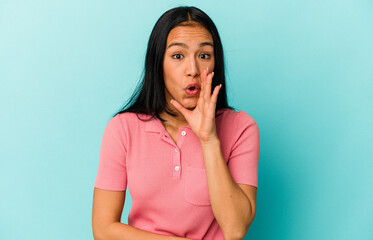 Young Venezuelan woman isolated on blue background is saying a secret hot braking news and looking aside