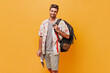© Look! - Cheerful modern man with ginger beard in grey t-shirt and printed shirt smiling, looking into camera and posing with large backpack..