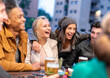 © MandriaPix - group of multi ethnic friends laughing and having fun during nightlife hangout, young woman and man drinking beers, evening party of erasmus students