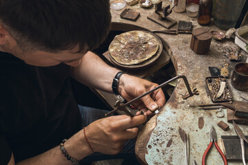 A jeweler saws a small piece of metal to repair a gold ring in his workshop