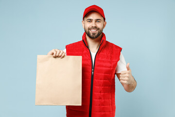 Wall Mural - Delivery guy employee man in red cap white T-shirt vest uniform work as dealer courier service hold brown clear blank craft paper takeaway bag mock up isolated on pastel blue color background studio.