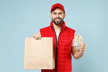 Wall Mural - Delivery guy employee man in red cap white T-shirt vest uniform work as dealer courier service hold brown clear blank craft paper takeaway bag mock up isolated on pastel blue color background studio.