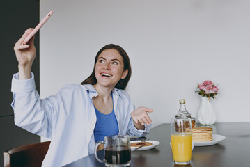 Wall Mural - Young fun housewife woman in casual clothes blue shirt eat breakfast do selfie shot mobile phone talk video call show pancakes cook food in light kitchen at home alone Healthy diet lifestyle concept