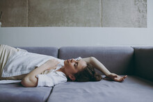Side View Young Carefree Relaxed Dreamful Caucasian Woman 20s Wearing Casual White Clothes Lying On Soft Grey Sofa Indoors Apartment Flat. Resting On Weekends Leisure Quarantine Staying Home Concept.