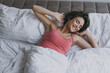 © ViDi Studio - Calm young fun happy positive caucasian woman 20s wearing pajamas lying on bed wrap covered under blanket duvet on pillow stretching resting relax at home. Good mood night morning bedtime concept