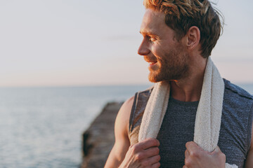 Close up happy young strong sporty athletic toned fit sportsman man in sports clothes towel warm up train look aside at sunrise sun dawn over sea beach outdoor on pier seaside in summer day morning