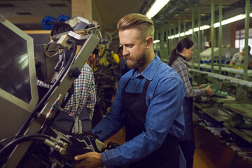 Side view of serious focused male shoe factory worker working with special industrial machinery while making new sneakers. Manufacturing industry and mass footwear production concept