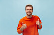 © Look! - Nice young man in good mood with ginger beard in cool sweatshirt smiling, looking into camera and posing on blue backdrop..