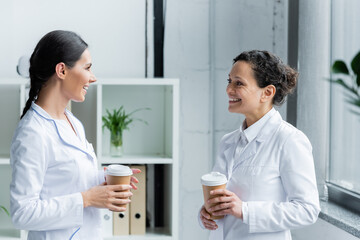 Wall Mural - Doctor with paper cup talking to african american colleague