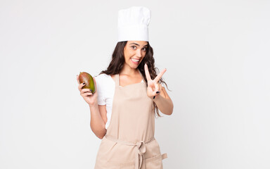 Wall Mural - pretty woman smiling and looking happy, gesturing victory or peace wearing an apron and holding a mango