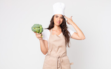 Canvas Print - pretty woman feeling confused and puzzled, showing you are insane wearing an apron and holding a broccoli