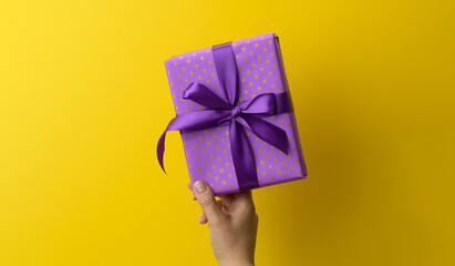 Wall Mural - female hand are holding a purole gift box on a yellow background