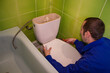 man repairs the toilet in the room,the man unscrews a drain tank of a toilet