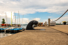 A Large Bollard At A Slip On A Harbour In Summer Time With Boats And Large Dreamy Clouds Behind It.  Banner