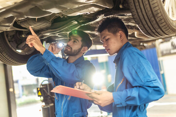 Two professional look technician inspecting car underbody and suspension system by using check list in moder car service shop. Automotive business or car repair concept.	