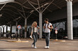 © Look! - Pretty blonde woman talks with brunette stylish man in white tee and jeans near airport. Cool girl in headphones and guy in sunglasses walks and holds backpacks.