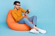 © deagreez - Portrait of attractive cheerful guy sitting in chair playing video game having fun free time isolated over bright blue color background