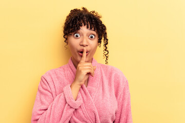 Wall Mural - Young mixed race woman wearing a pink bathrobe isolated on pink background keeping a secret or asking for silence.