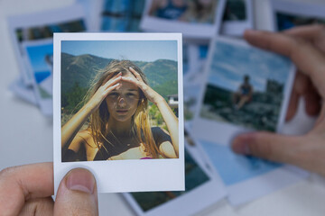 A person holds a polaroid photo in his hands against the background of other photos. Photo in hand close-up. A person looks at a photo from a polaroid.