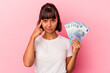 © Asier - Young mixed race woman holding bills isolated on pink background pointing temple with finger, thinking, focused on a task.