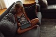 Young girl, sits on the couch and watchs on tablet. Child using gadget. Kid watching tablet.
