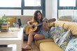 © Jake Jakab - young woman sitting in modern apartment on couch playing guitar