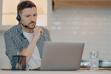 Young bearded man using headset and laptop while working at home