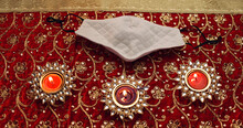 Top View Of Three Ornamental Lit Candles And Headress On Red Clothing With Brooches
