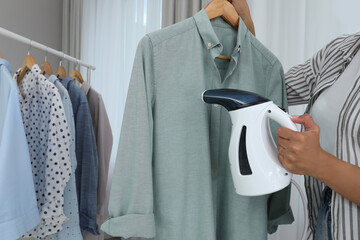 Wall Mural - Woman steaming shirt on hanger at home, closeup