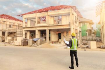 young professional engineer in protective helmet and blueprints paper at the house building construction site