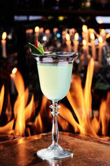 yellow green cocktail with gin and lime in a beautiful glass on copper designer bar counter, the background of real fire. Series of photo. High quality photo