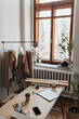© Look! - Photo of light working office. Snaphot of white room with wooden window, table, coffee cup, hanger with paper clothes patterns