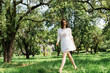 Cheerful woman in summer dress walking on grass in park