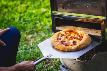 Wall Mural - High angle shot of a male taking ready pizza out of oven outdoors