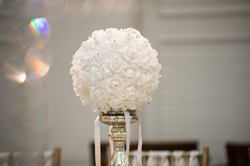 White round faux flower in glass cylinder vase with silver base centerpiece at wedding reception table setting on white background