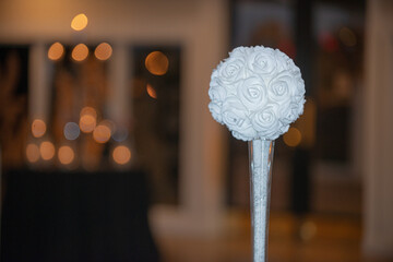 Wall Mural - White round faux flower in glass cylinder vase centerpiece at wedding reception table setting with warm bokeh background