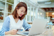 © Ekkasit A Siam - Portrait A beautiful Asian woman in a white shirt sitting in a bakery shopping online with her credit card and laptop computer in front of her hands.