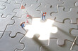 Miniature worker stand on white jigsaw puzzle with missed and shining piece. Solution concept.