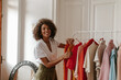 © Look! - Beautiful curly young dark-skinned woman in white blouse and khaki shorts smiles sincerely, looks into camera and poses in dressing room.