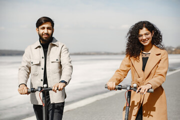 Wall Mural - Interracial young couple with scooters in the city background