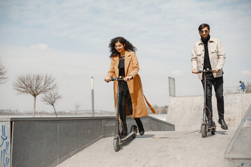 Wall Mural - Interracial young couple with scooters in the city background