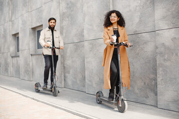 Wall Mural - Interracial young couple with scooters in the city background