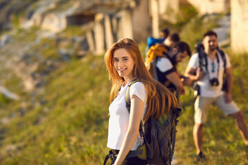 Wall Mural - portrait of a happy beautiful red-haired hiker girl with a big backpack who travels with friends in 